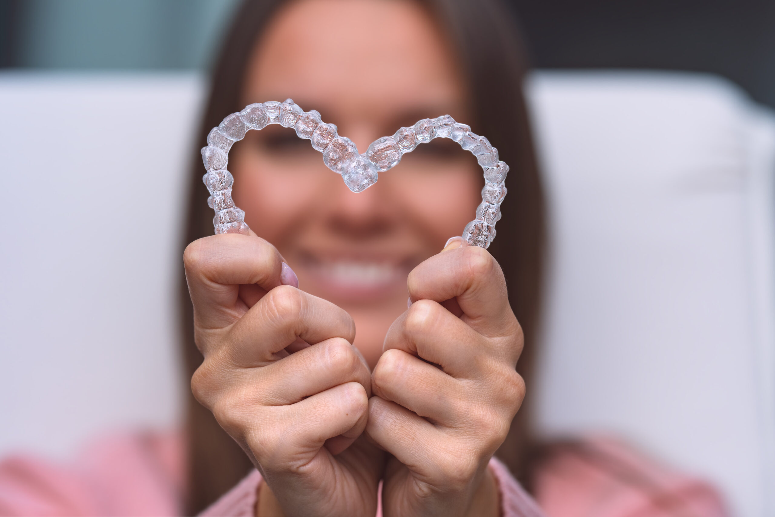 Eine Junge Frau, die zwei Invisalign-Schienen in Herzform zusammengelegt vor die Kamera hält.