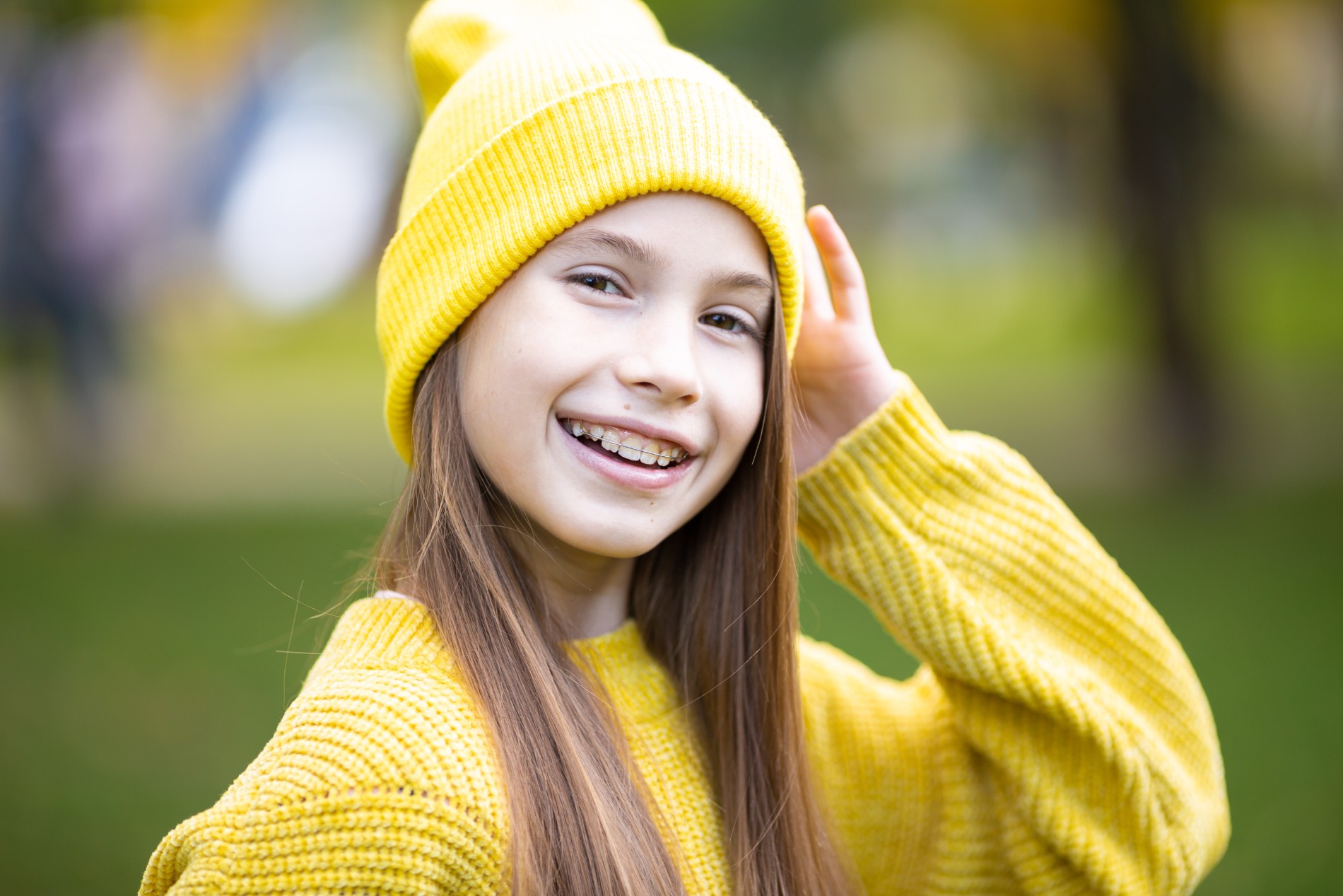 Portrait of modern happy teen girl with dental braces dressed in yellow clothes in park. Pretty teenage girl wearing braces smiling cheerfully. Kid girl in autumn smiling with braces teeth apparatus