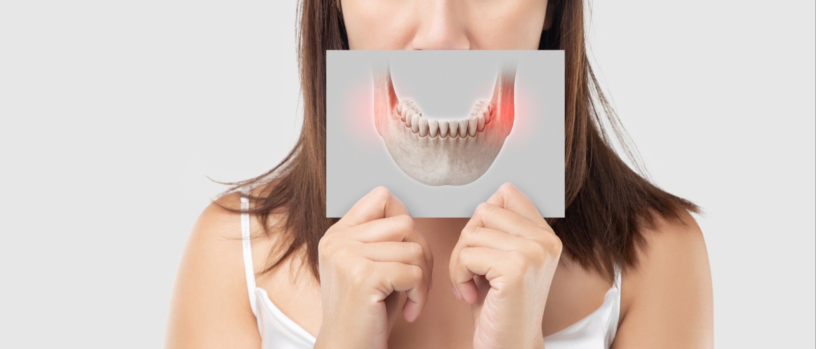 blog-kiefer-chronisch-entzündet – Kopie Eine junge Frau hält eine schematische Aufnahme eines Kiefers vor ihr Gesicht. Auf der Aufnahme sieht man entzündete Muskelstränge.